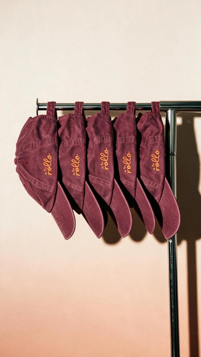 Five washed burgundy caps embroidered with the a tu rollo logo, hanging from a chrome rail